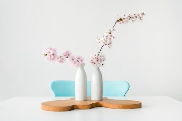 Deux vases blancs avec des fleurs de couleurs pastel posé devant une chaise au dossier bleu pastel.