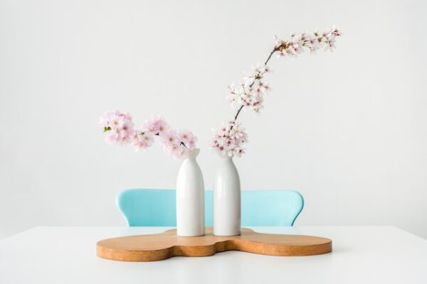 Zwei weiße Vasen mit pastellfarbenen Blumen stehen vor einem Stuhl mit pastellblauer Rückenlehne.