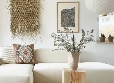 Un salon à la déco bohème avec un canapé de couleur claire, une déco murale en jute et des fleurs séchées dans un vase en bois.