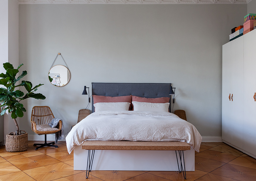 Schlafzimmer mit Blick auf das Bett, einen weißen Kleiderschrank, Parkettboden, einen Feigenbaum und dekorative Kissen und Decken