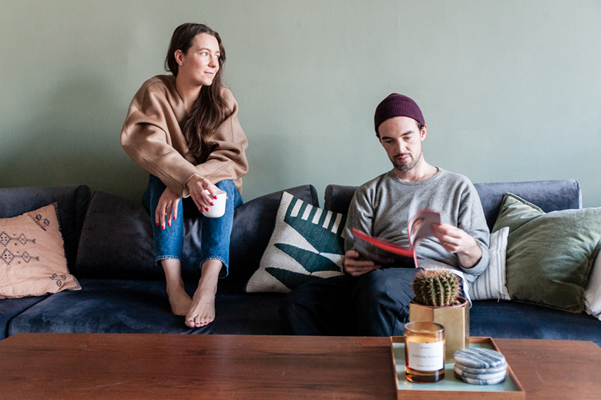 Ariane avec une tasse à la main et Rainer lisant un magazine dans leur canapé MYCS