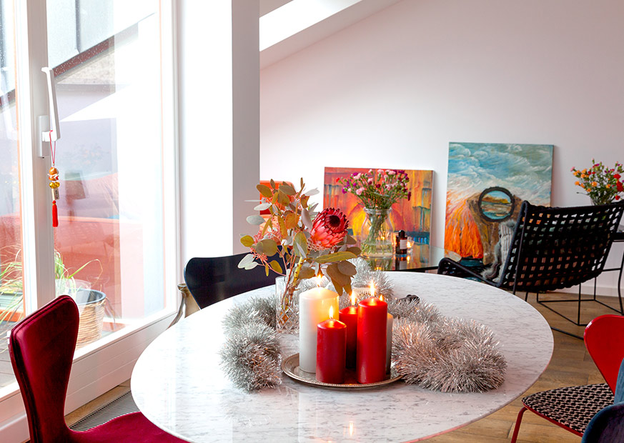 Blick auf den Esstisch mit Kerzen, Blumenvase und silberner Dekoration, im Hintergrund Ölgemälde